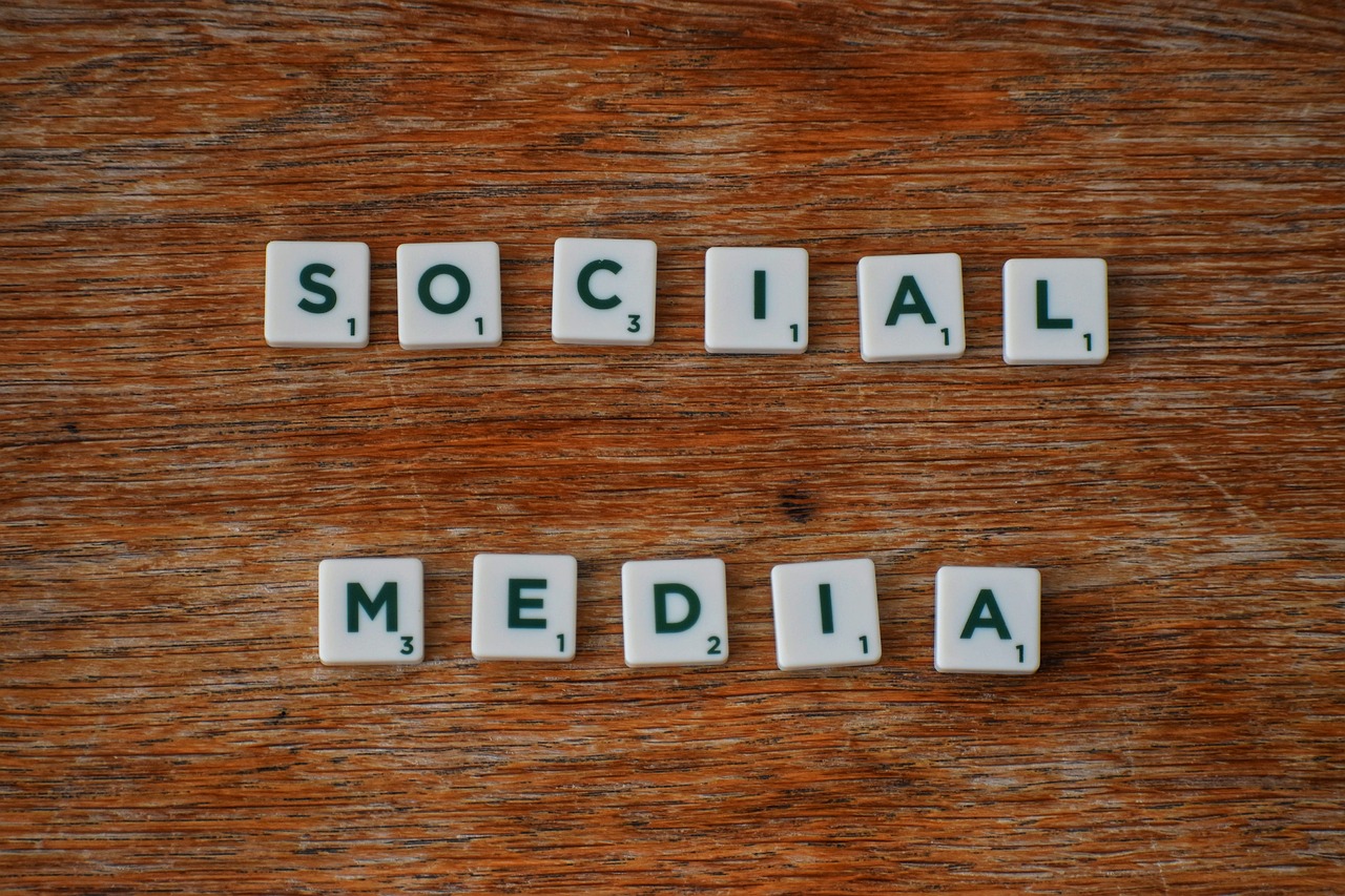 Picture of the words "social media" spelled out in Scrabble tiles. The tiles are on a wooden table.
