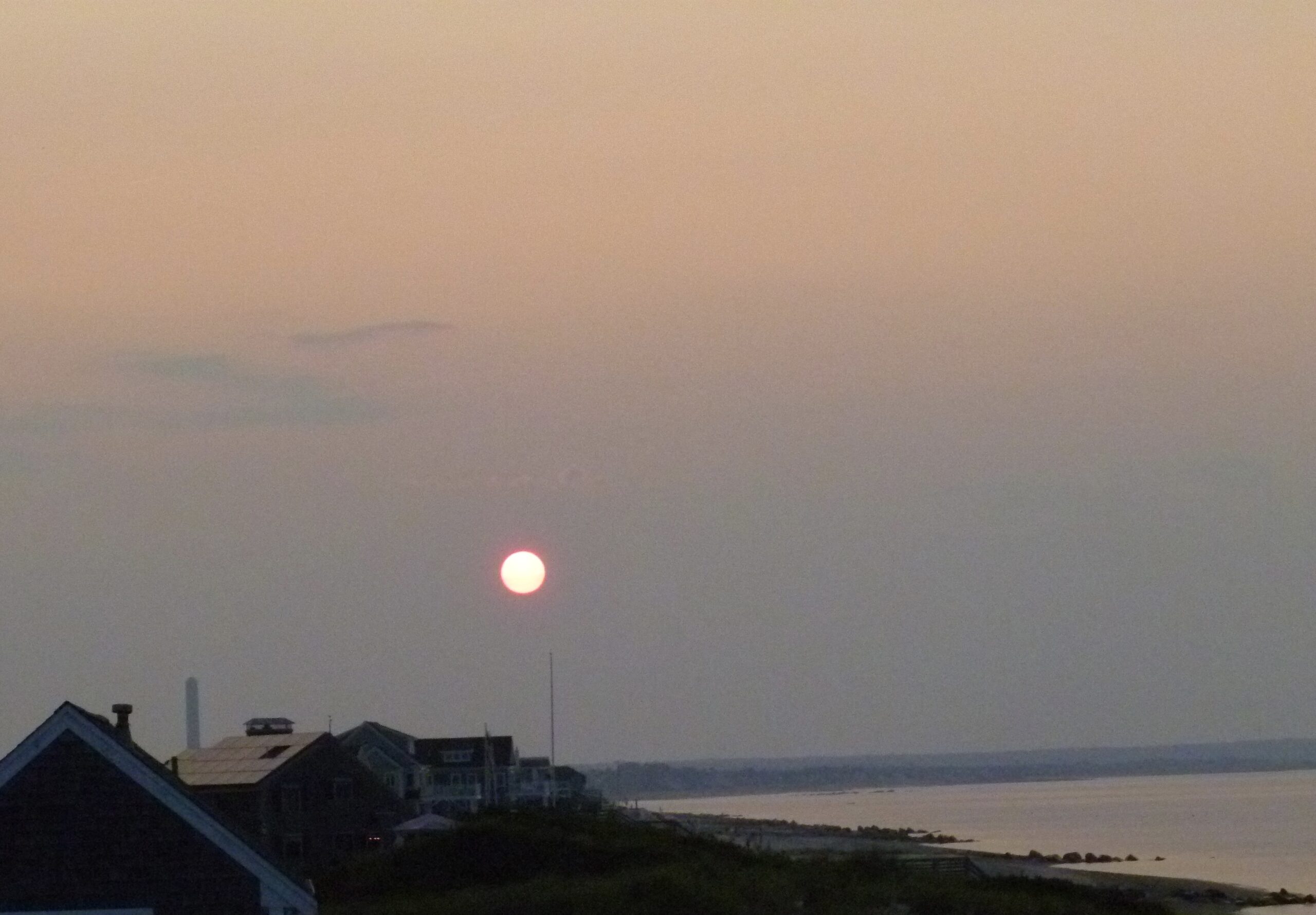 Picture of the sunset on a beach with houses along the coastline. 